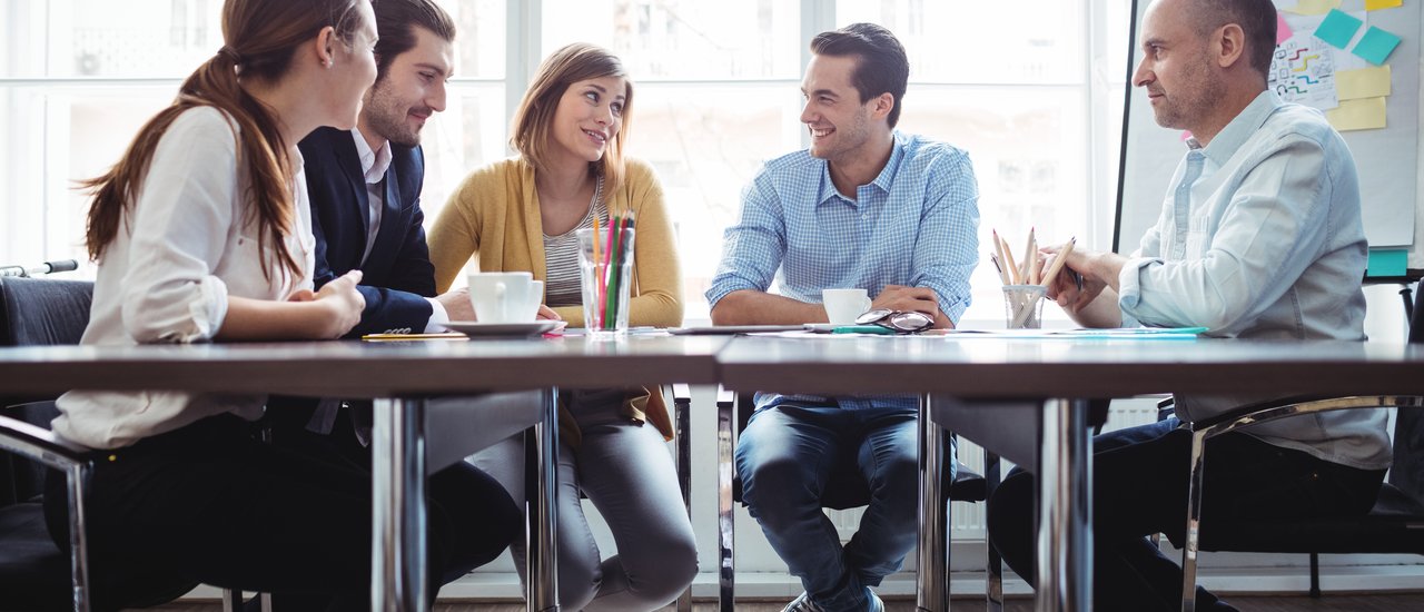 Five people are sitting around a desk in an office and talk about business.